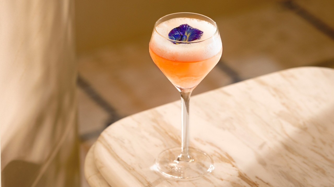 Glass of cocktail in pink decorated with a blue flower served at Maison Boulud, a waterfront bar in Singapore
