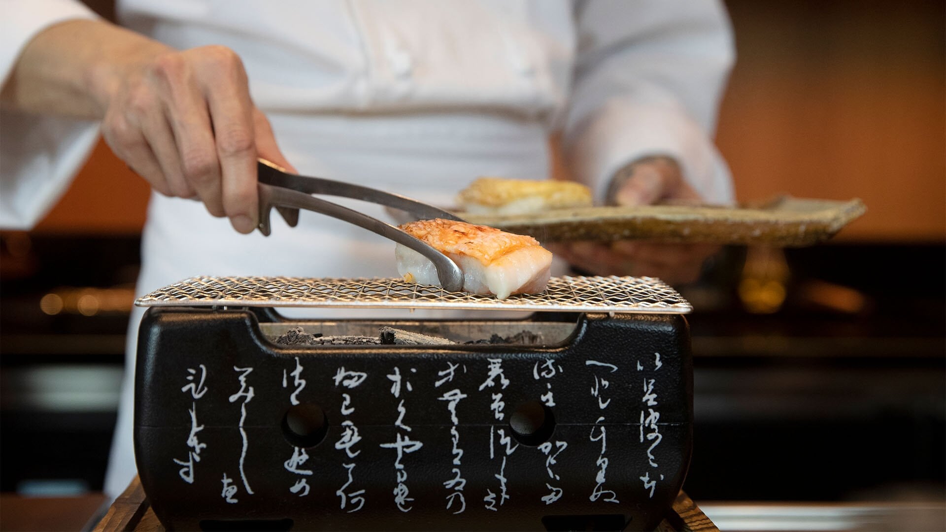 Chef grilling fish over charcoal for an omakase meal