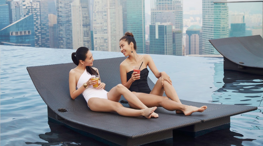 Two women in swimwear, enjoying drinks at the Infinity Pool in Singapore