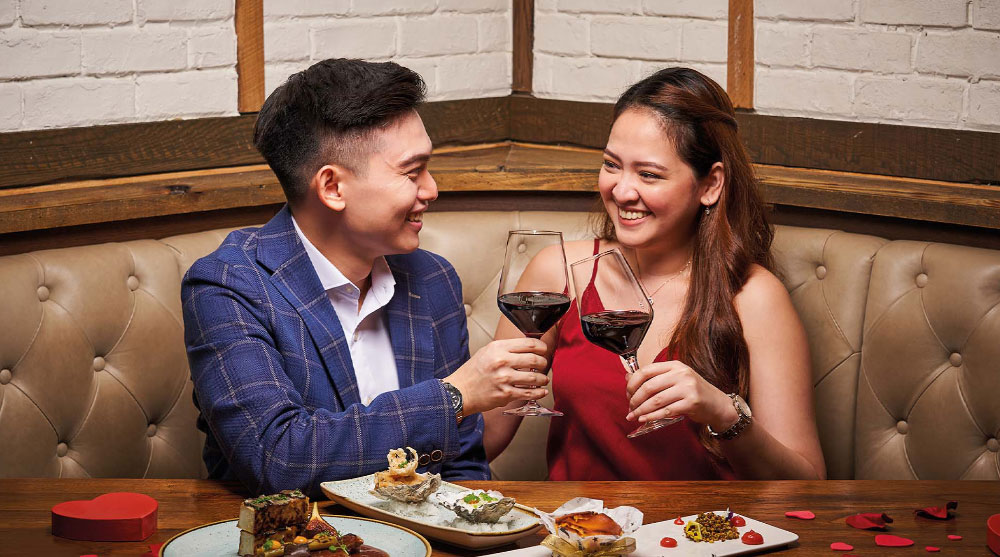 Man and woman smiling at each other while preparing to toast over red wine at a Valentine's day dinner