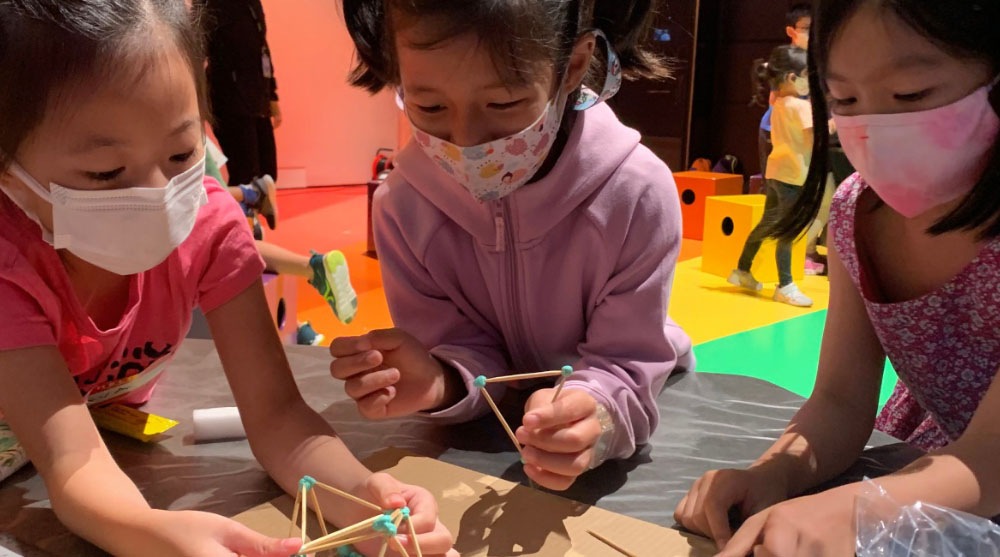 3 kids enjoying a hands-on activity with wooden sticks at a creative holiday programmes at ArtScience Museum