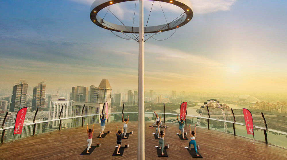 People enjoying a yoga retreat experience at SkyPark Observation Deck while overlooking downtown Singapore